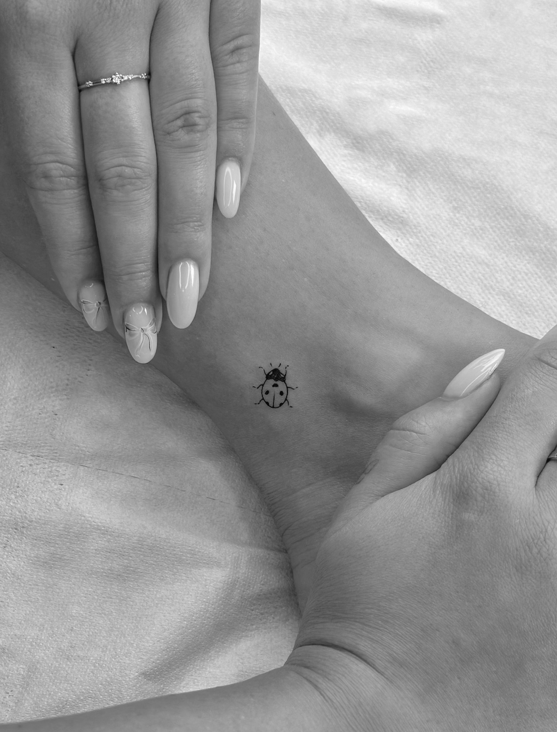 Ladybug ankle tattoo with manicured hands on a soft surface Ladybug ankle tattoo with manicured hands on a soft surface